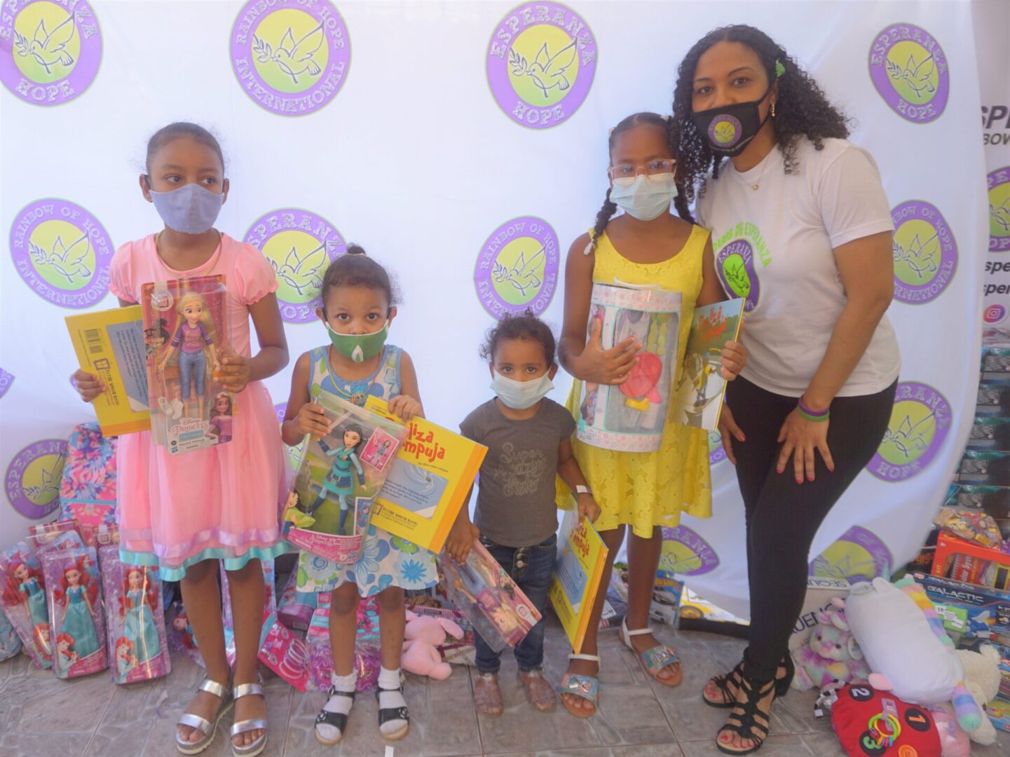 A staff and four girls standing against the Esperanza-Hope backdrop with their toys and books