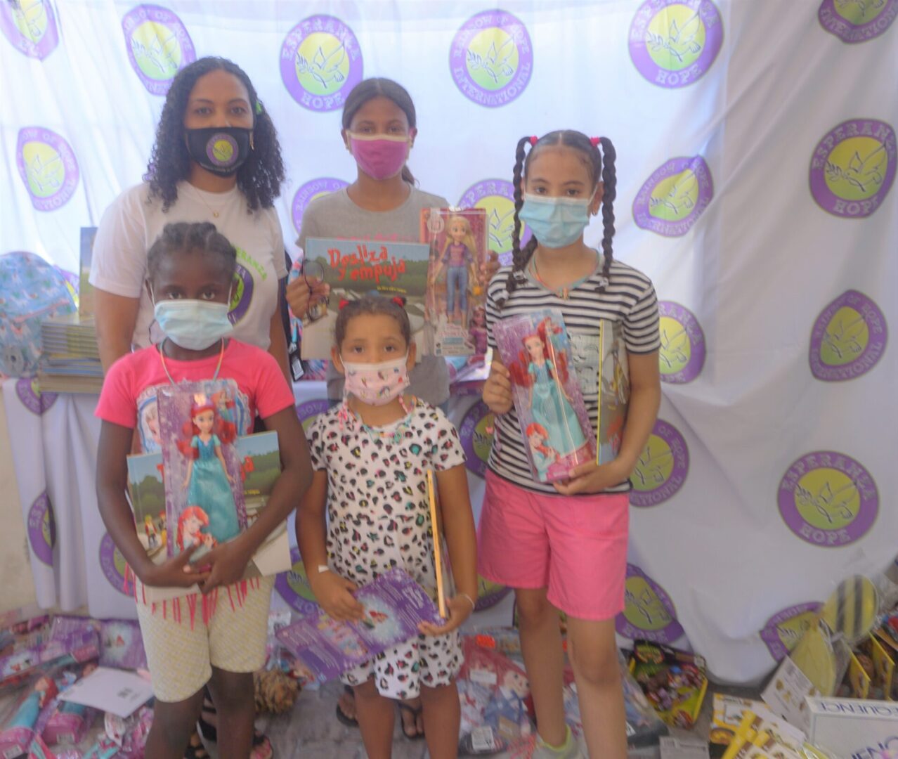Our staff and four girls standing against the Esperanza-Hope backdrop with their toys and books