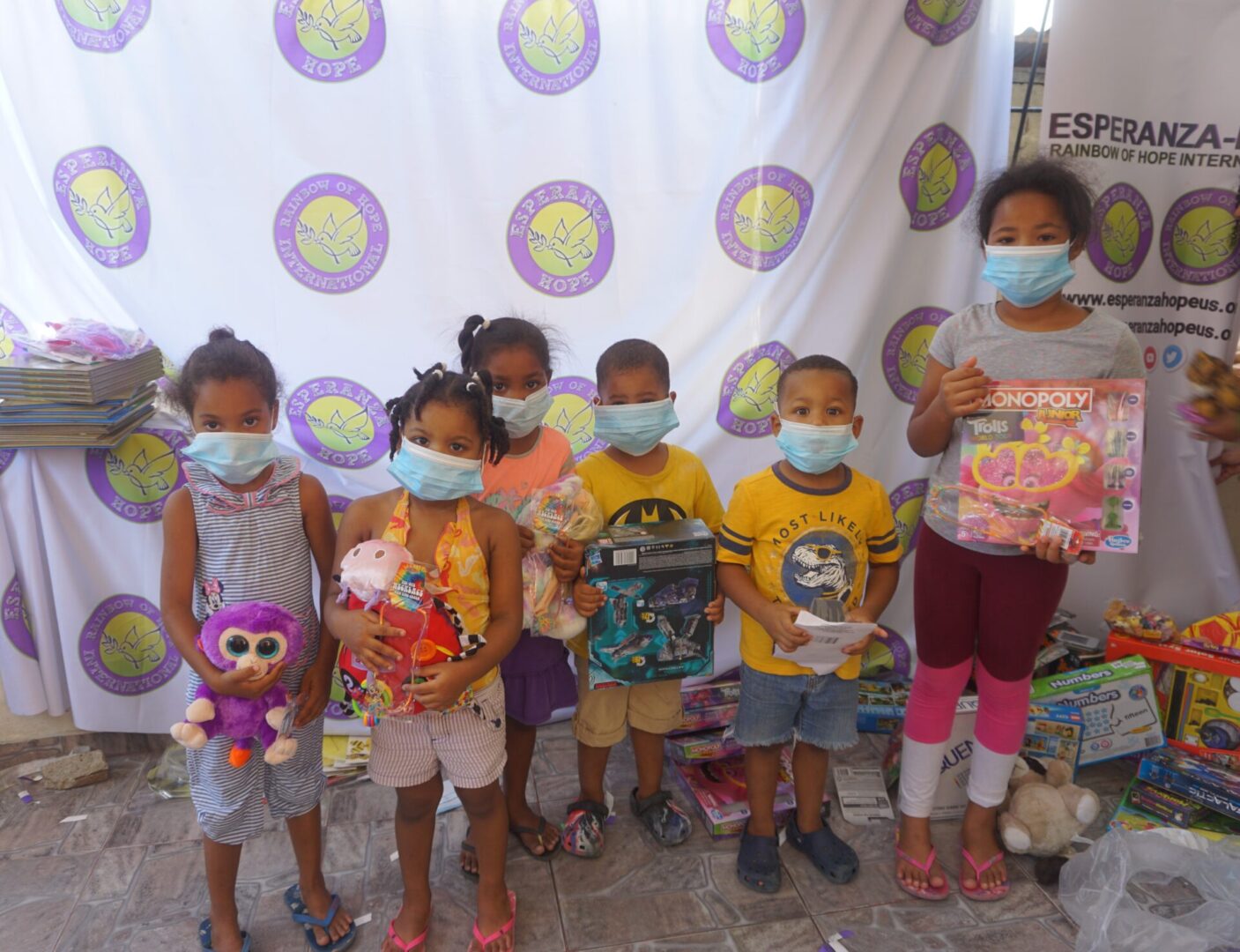 Six children standing against the Esperanza-Hope backdrop with their toys and books