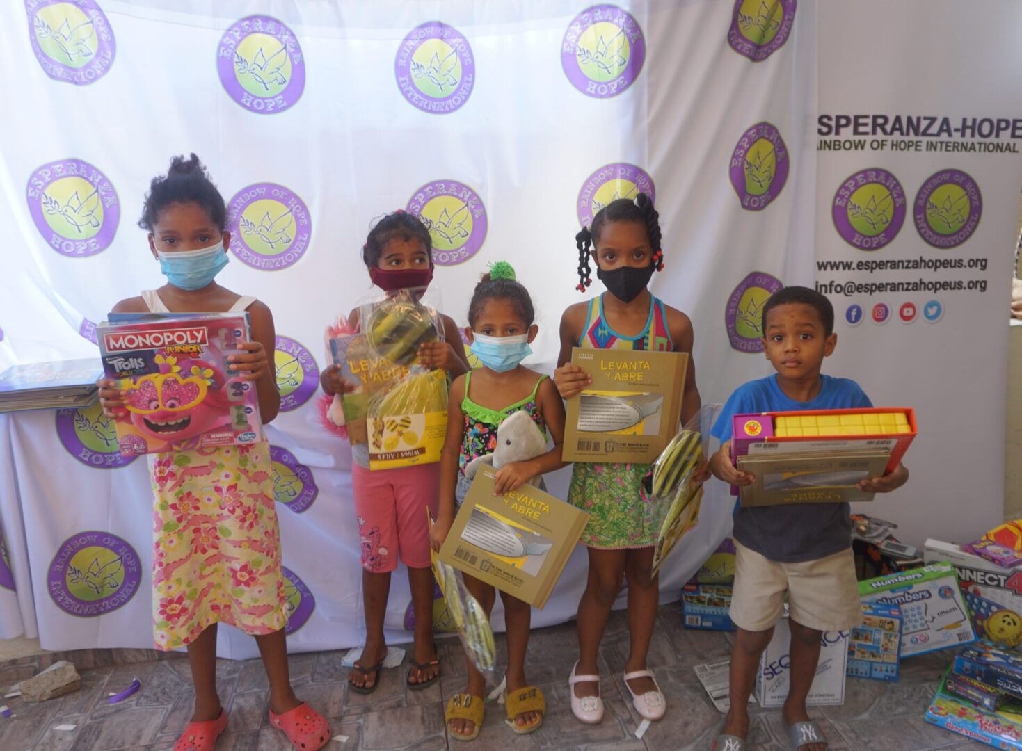 Five children standing against the Esperanza-Hope backdrop with their toys and books, batch 7