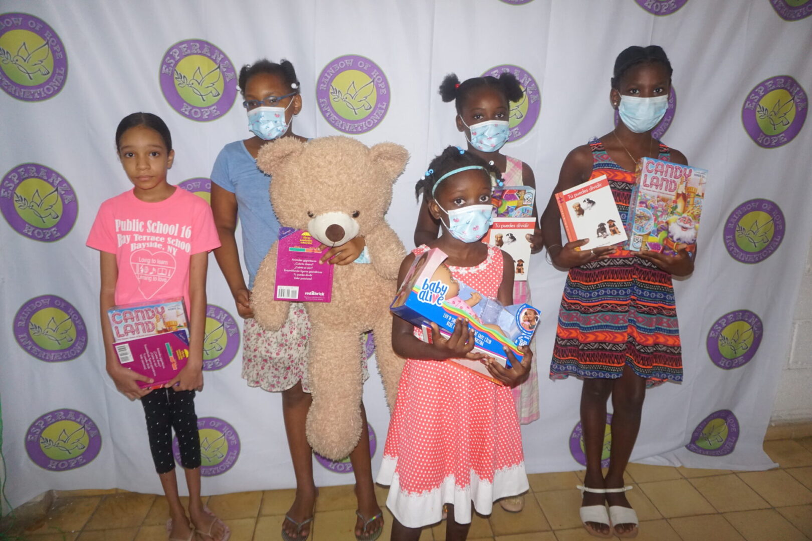 Five girls, each holding a toy and a book, standing against the Esperanza-Hope backdrop