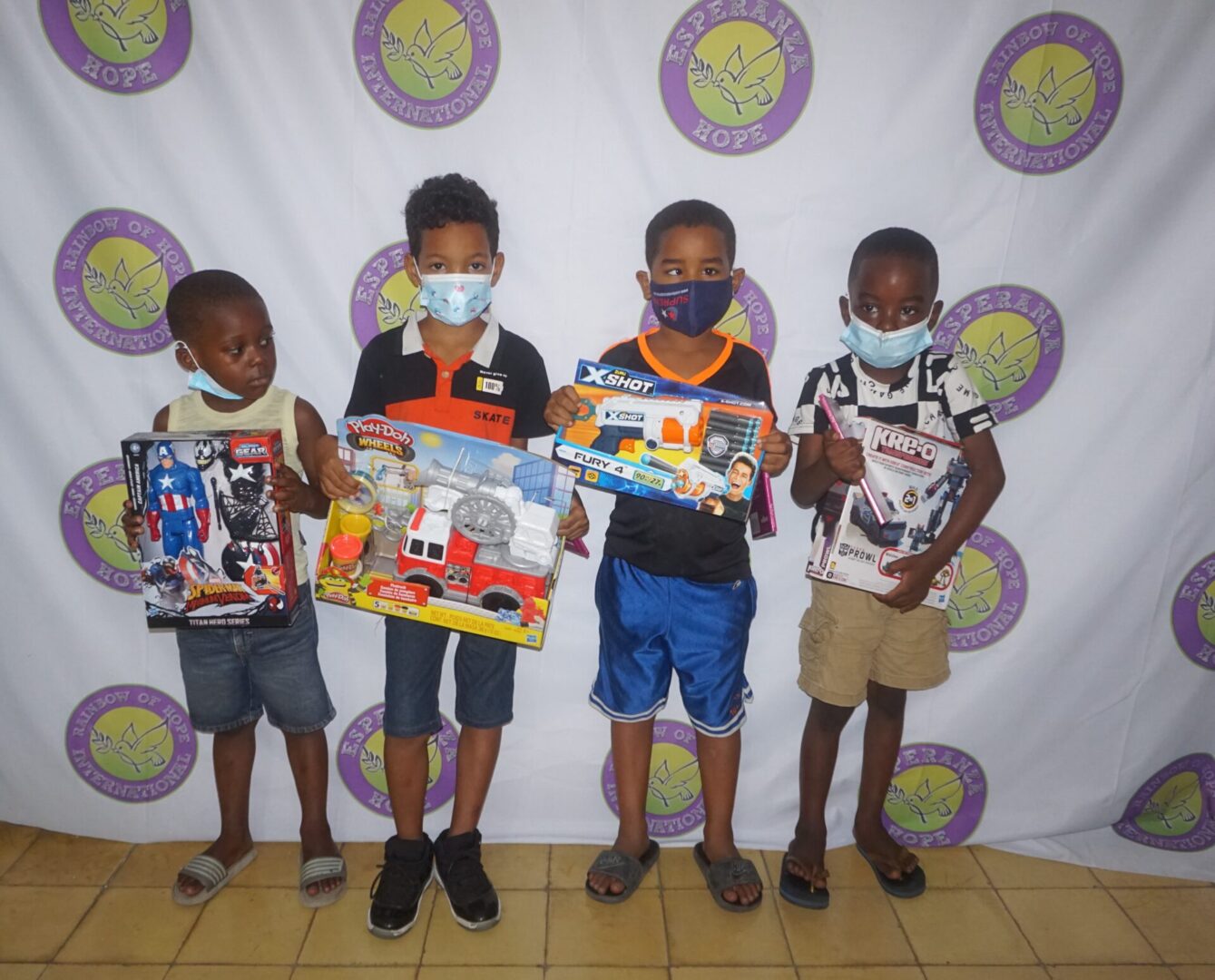 Four boys holding toys against the Esperanza-Hope backdrop, batch 4