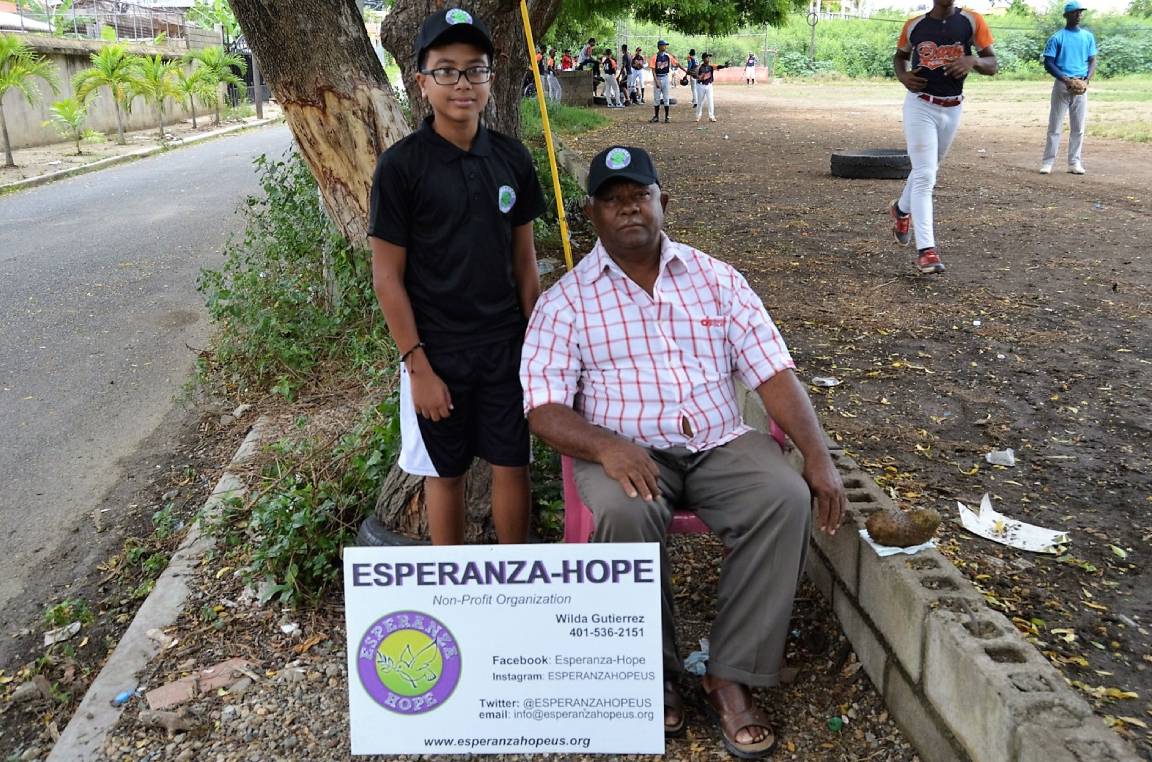 A boy with glasses and a man sitting, with our org’s placard on their feet