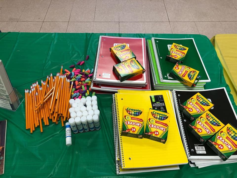 School supplies including pencils, erasers, glue sticks, and Crayola crayons arranged on a table.